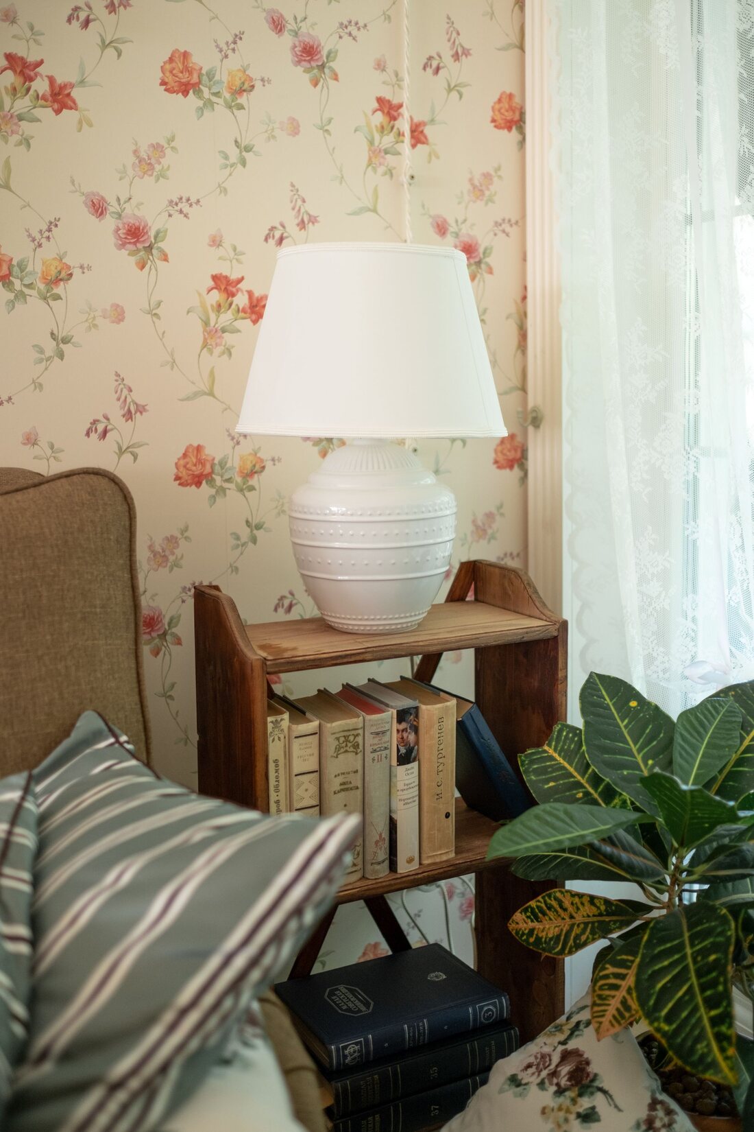 Cozy reading nook with soft floral wallpaper, a table lamp and stacked books