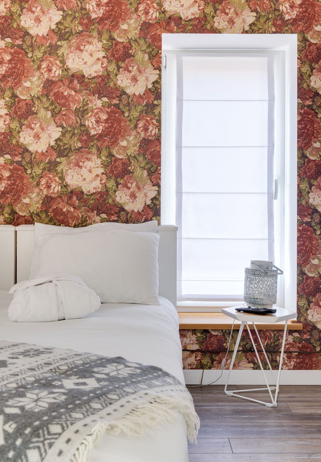 Bedroom with bold burgundy floral wallpaper beside a bright window and white bedding