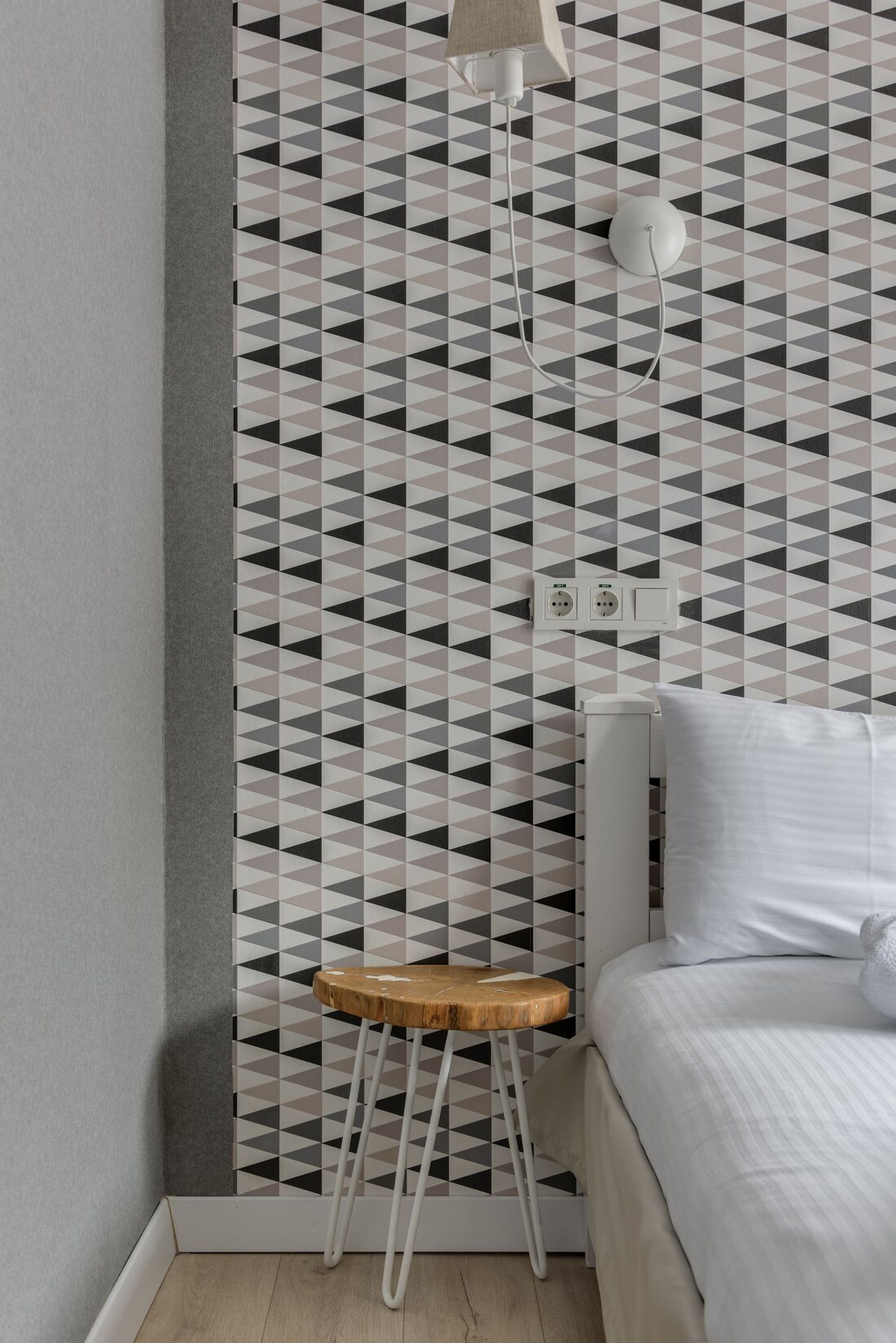 Bedroom corner with black and white geometric triangle wallpaper and a white bed