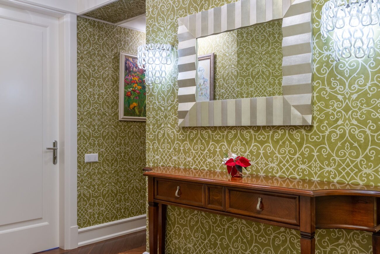 Hallway lined with green damask wallpaper, a framed mirror and a console table