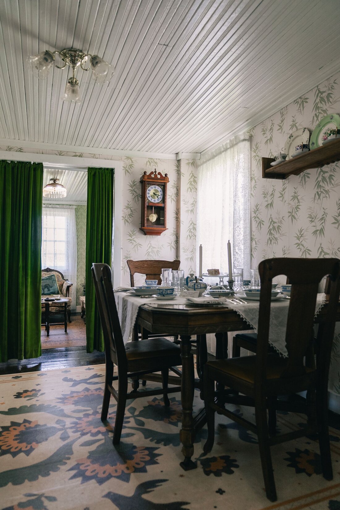 Vintage dining room with floral wallpaper, green drapes and an antique table set for a meal