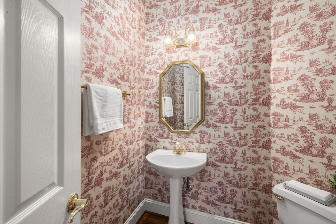 Powder room wrapped in red toile chinoiserie wallpaper with a pedestal sink and octagonal mirror