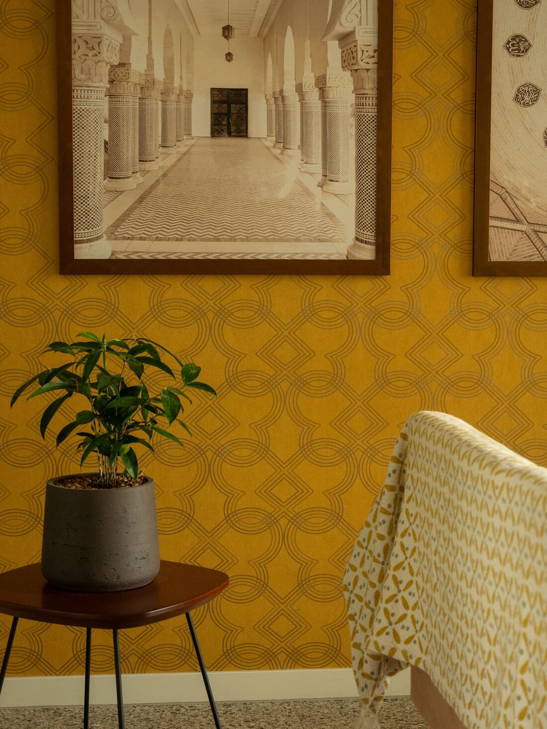 Living-room corner with mustard-yellow geometric wallpaper, a potted plant and an upholstered chair