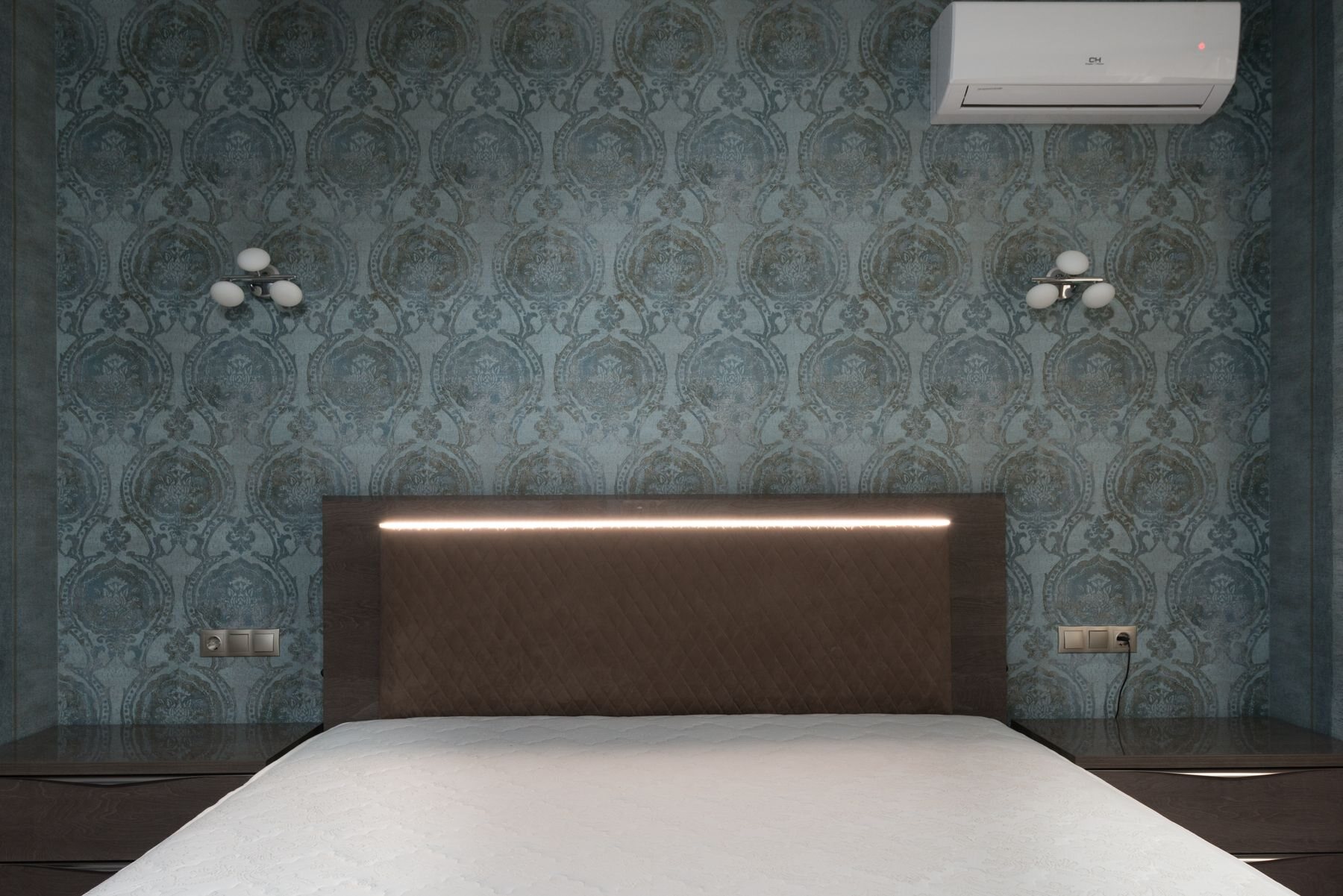 Elegant bedroom with deep teal damask wallpaper installed behind the headboard and framed by wall sconces