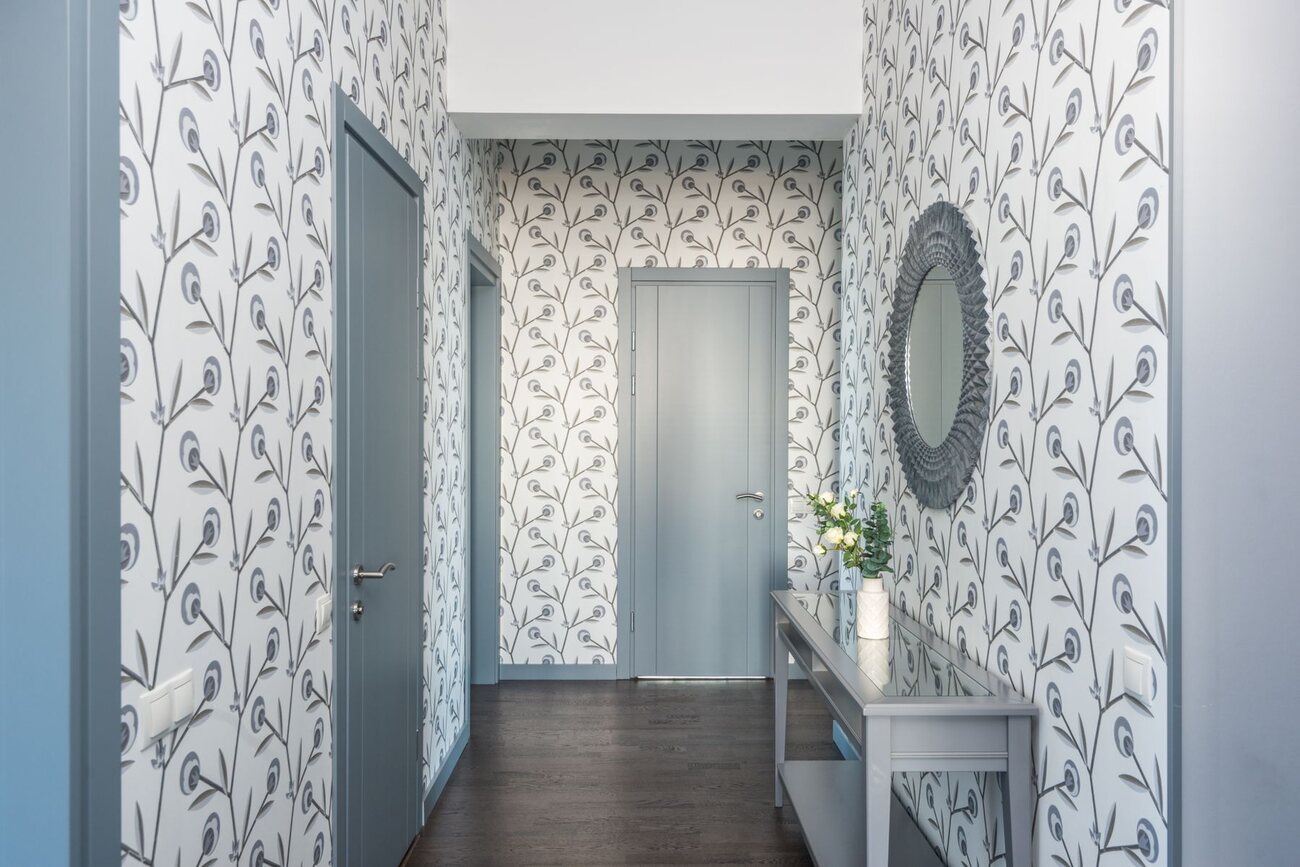 Bright entryway lined with blue and white botanical wallpaper, a round mirror and a console table
